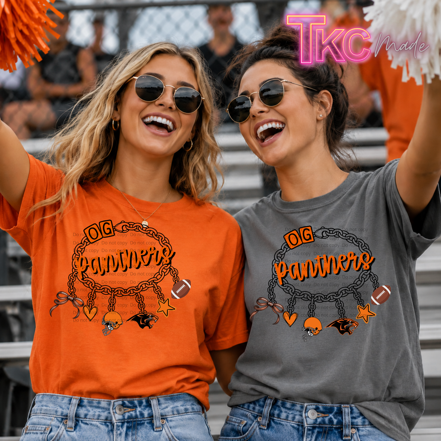 Two women in a stadium wearing matching graphic T-shirts. The woman on the left wears a bright orange shirt with a black and orange 'OG Panthers' chain graphic, and the woman on the right wears a dark gray shirt with the same graphic.