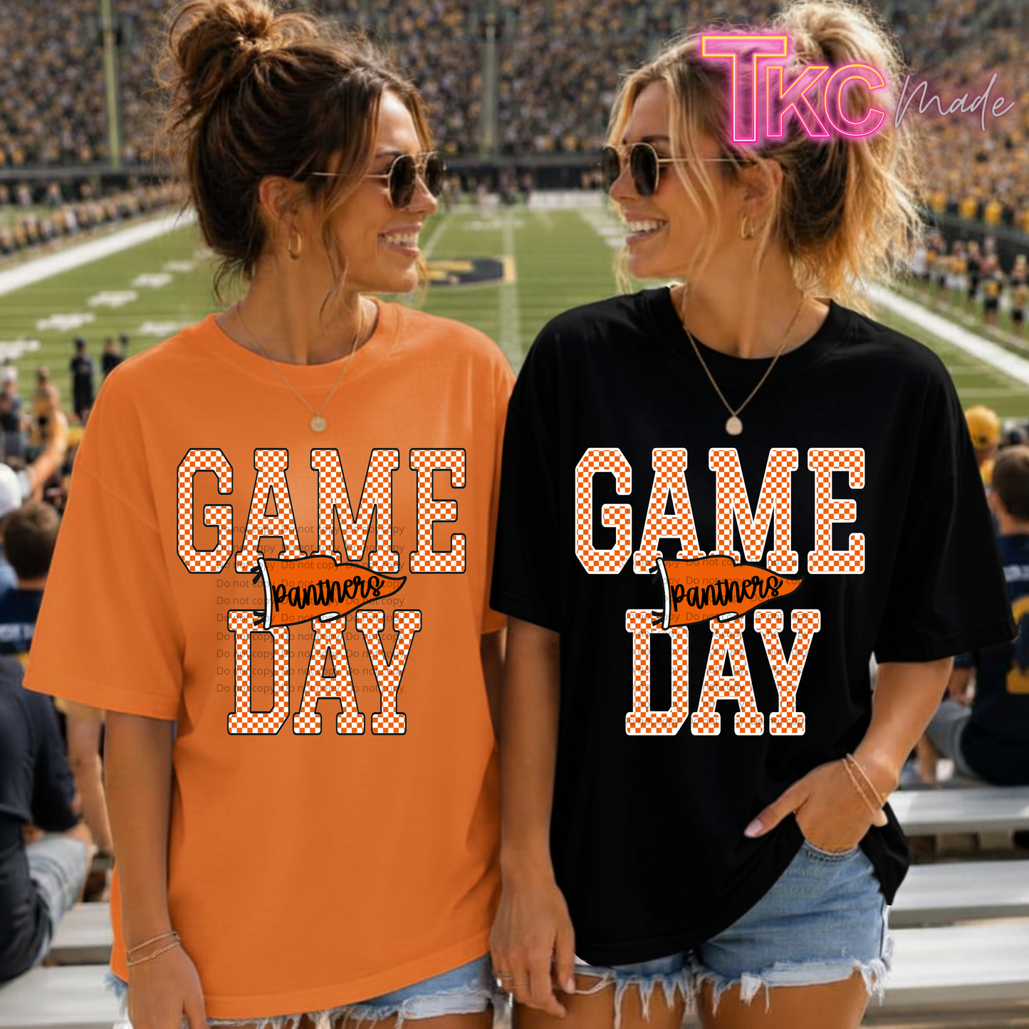 Two women standing in a football stadium, wearing matching 'GAME DAY Panthers Day' graphic t-shirts, one in orange and one in black. A 'TKc Made' watermark is visible in the top right corner.