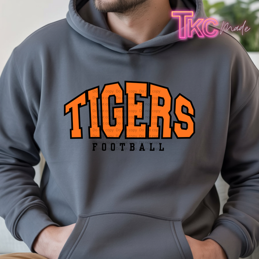 A man wearing a dark gray hoodie with 'TIGERS FOOTBALL' printed in orange and black on the front. The photo is cropped from the chin down, showing the chest, hood, and hands in the pocket.