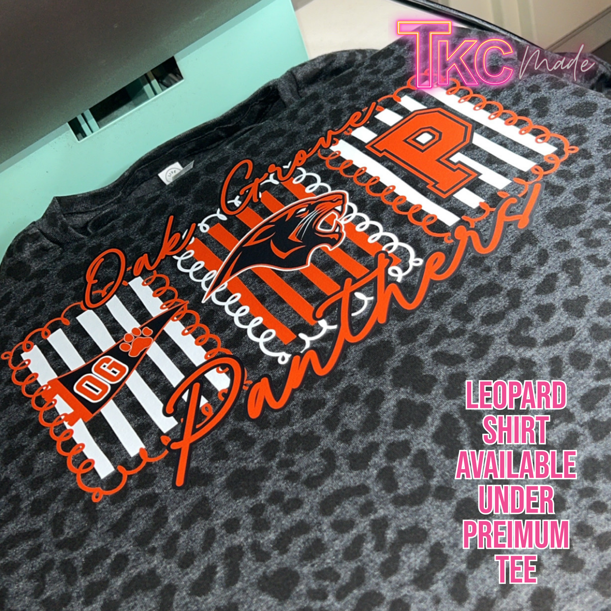 A close-up of a dark gray leopard-print t-shirt featuring a large custom graphic design in orange, white, and black. The design includes the text 'Oakley Custom Panthers', a panther graphic, and 'PAG' with a paw print.