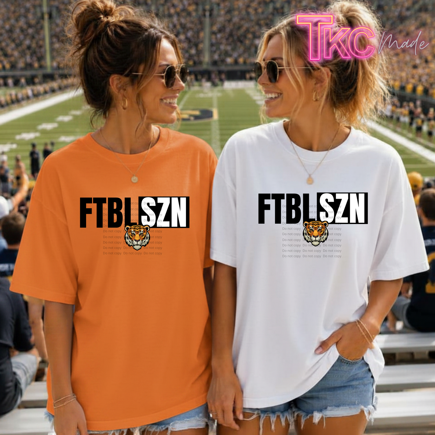 Two women standing on a football field wearing oversized graphic t-shirts. The woman on the left wears an orange t-shirt with 'FTBLFSZN' and a tiger graphic, and the woman on the right wears a white t-shirt with the same graphic.