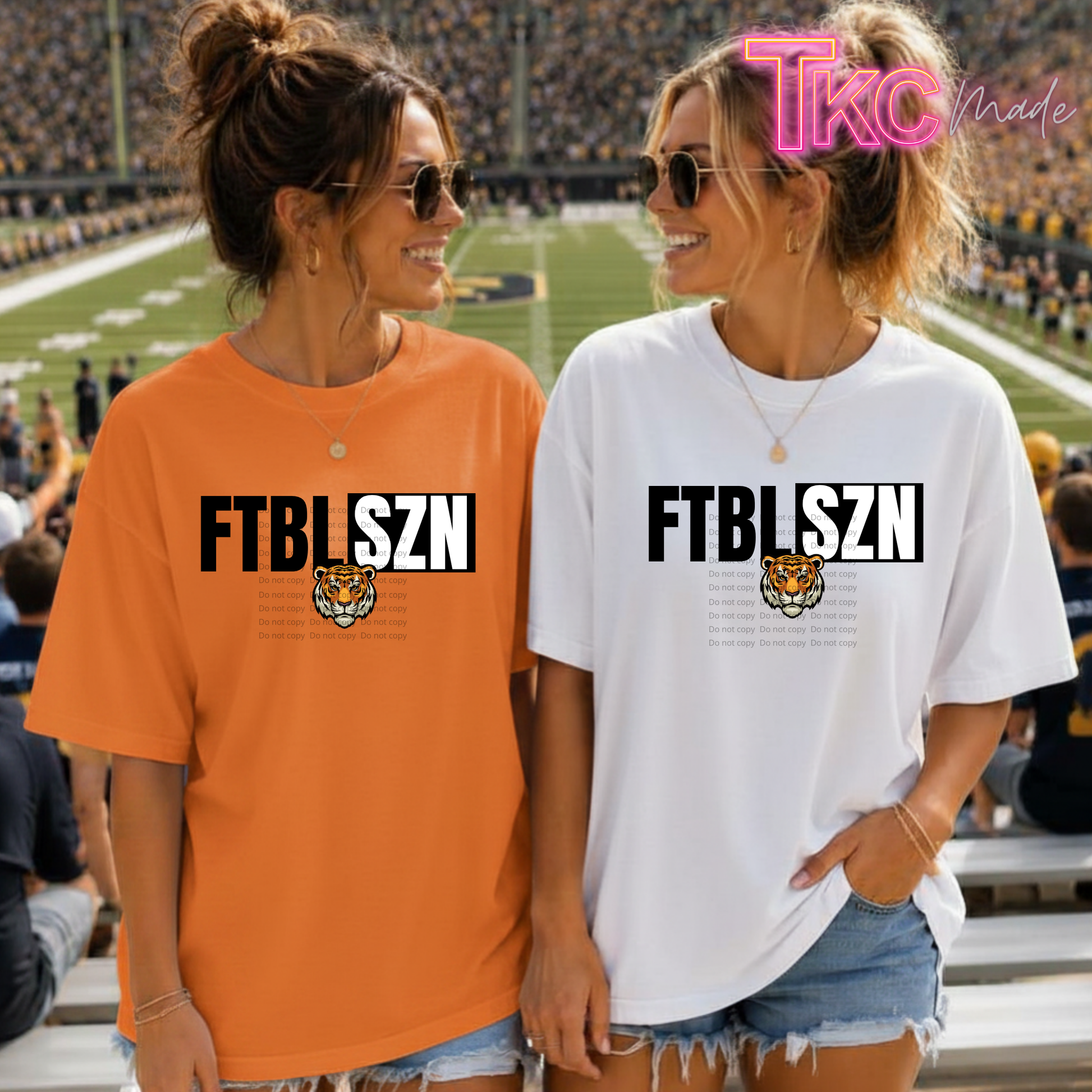 Two women standing on a football field wearing oversized graphic t-shirts. The woman on the left wears an orange t-shirt with 'FTBLFSZN' and a tiger graphic, and the woman on the right wears a white t-shirt with the same graphic.
