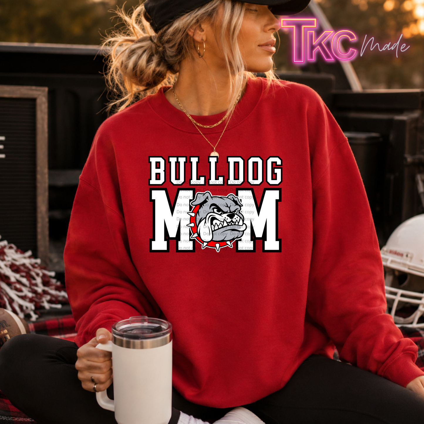 A woman wearing a red sweatshirt with a white and gray bulldog graphic and the words 'BULLDOG MOM' sits in a truck bed holding a white mug. A 'Tkc Made' watermark is visible in the top right corner.