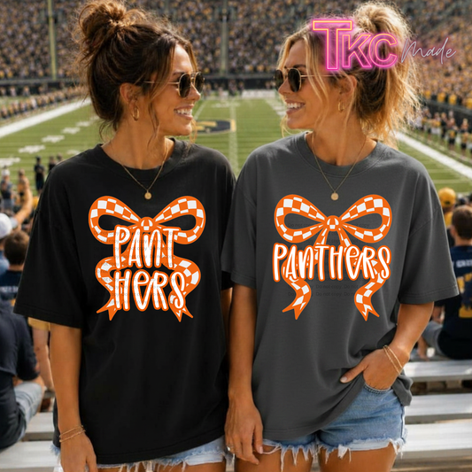 Two women standing in a stadium wearing matching graphic T-shirts. The shirt on the left is black with an orange and white checkered bow and the text 'PANTHERS', and the shirt on the right is dark gray with the same graphic.