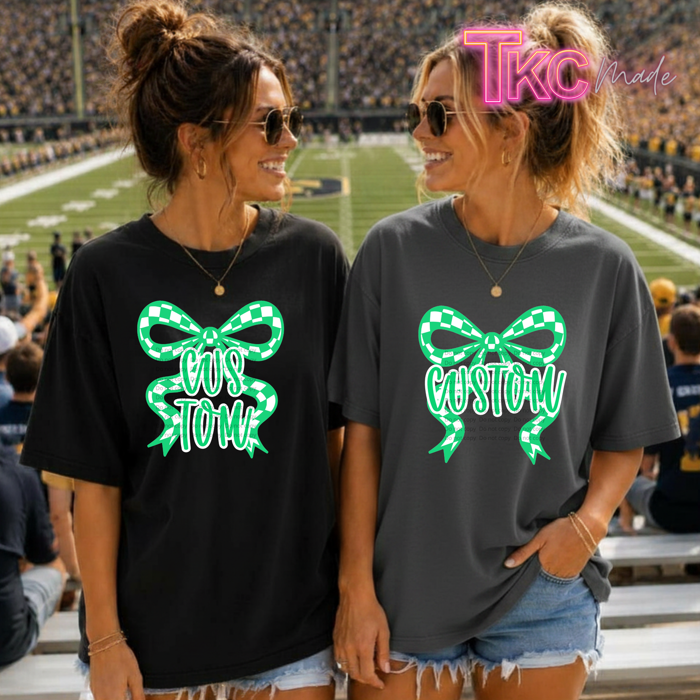 Two women standing in a stadium wearing oversized graphic t-shirts. The shirt on the left is black with a green and white checkered bow graphic containing the text 'COST TOM'.