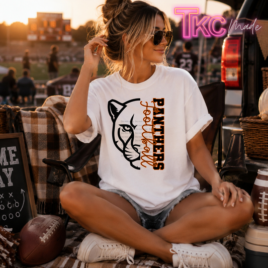 A woman sitting cross-legged outdoors at a football game wearing a white graphic T-shirt with a black panther illustration and the words 'PANTHERS football' in black and brown. The scene includes a truck, football, plaid blanket, and warm sunset lighting.