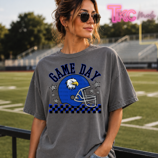 A woman wearing a gray graphic t-shirt with a blue and white football helmet design and the words 'GAME DAY' on the front, standing on a sports field.