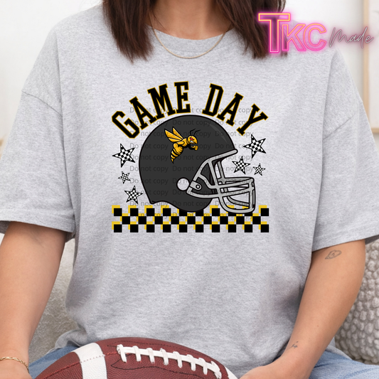 A person wearing a gray shirt with a large grey, black and gold football graphic that reads "GAME DAY" and shows a hornet on a helmet. The person is sitting on a couch holding a football.