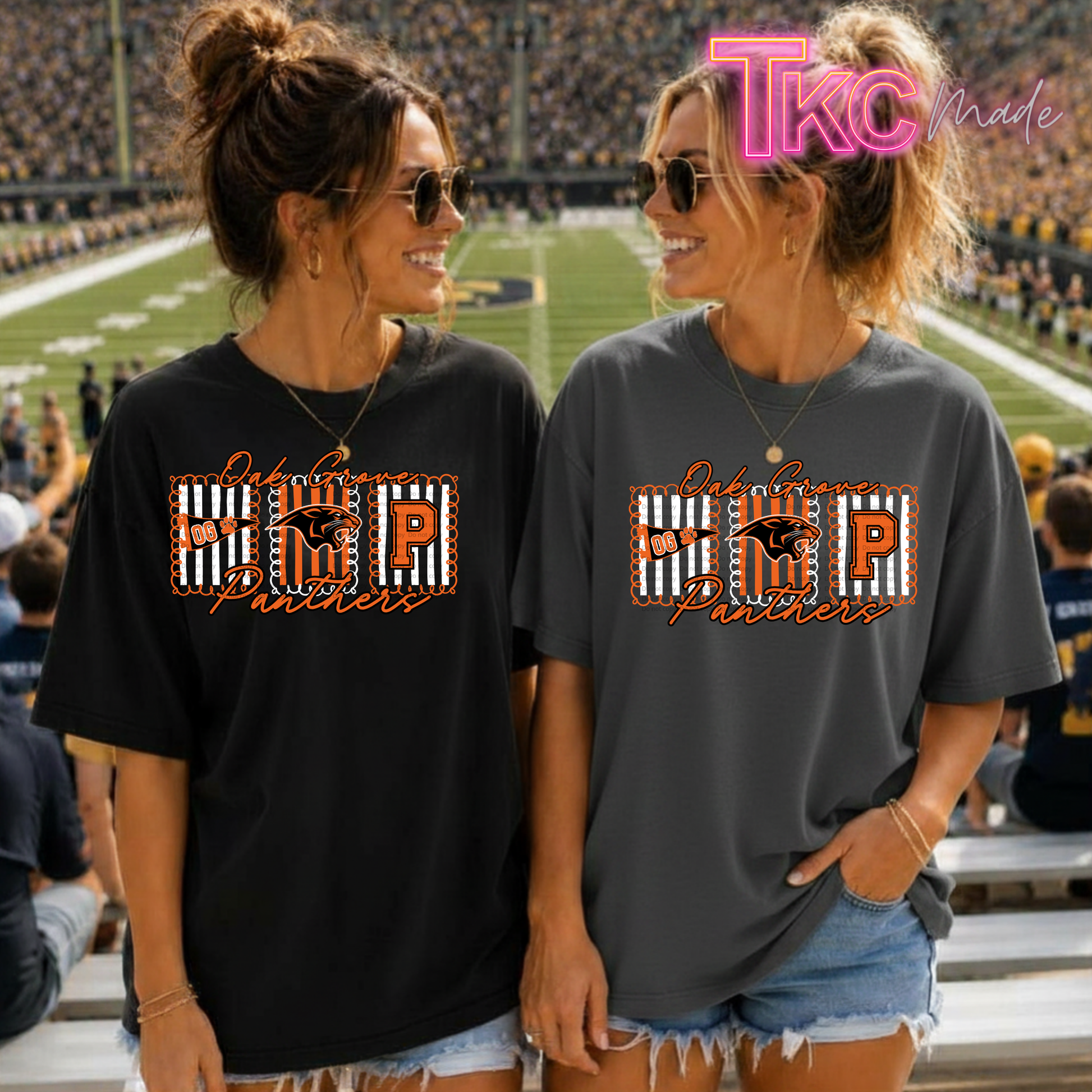 Two women standing in a stadium wearing matching graphic T-shirts. The shirt design features a large block letter 'P' with a stripe pattern, the letters 'OG', and the words 'Oak Grove Panthers' in orange script.